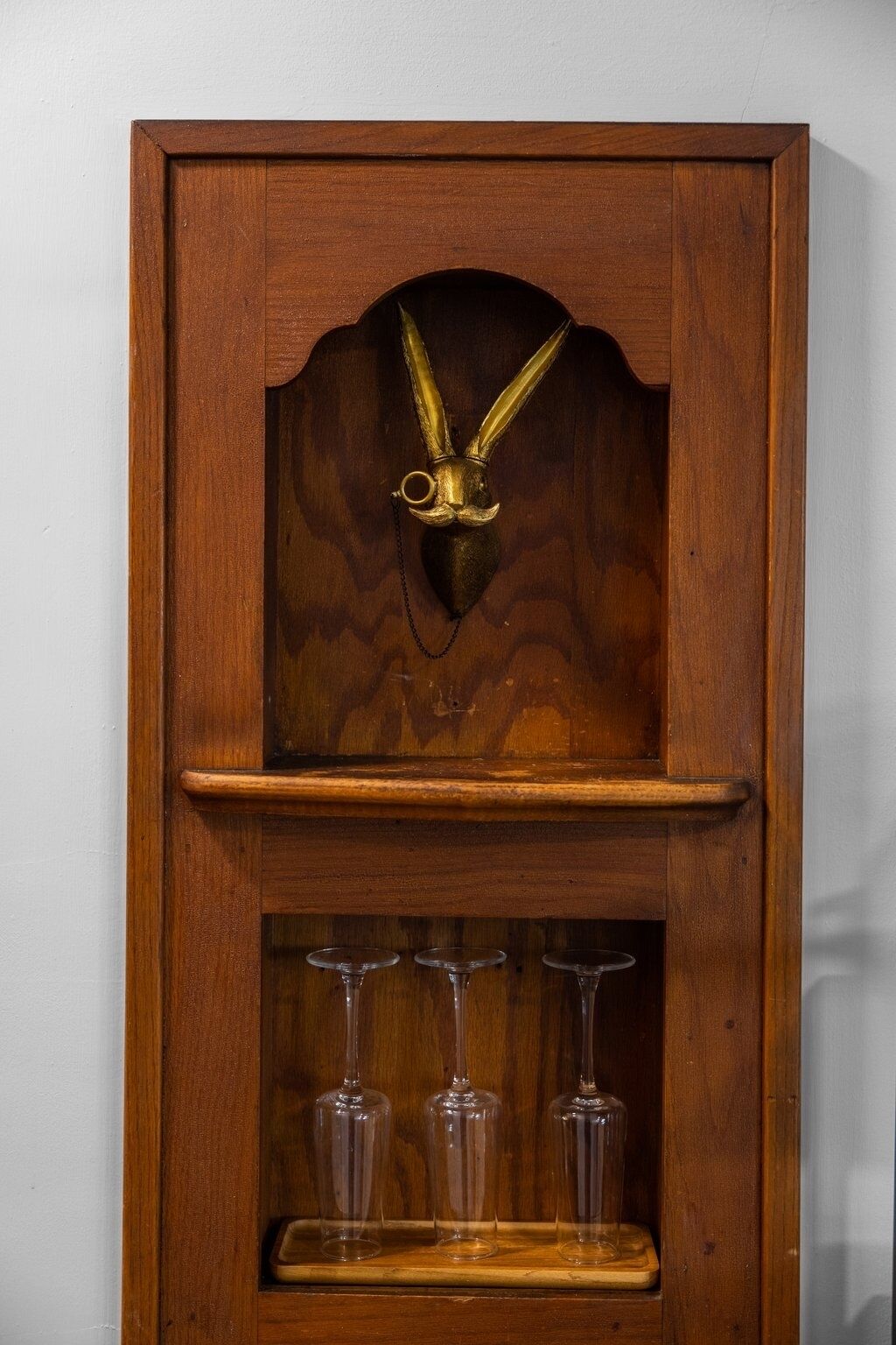 Un meuble en bois orné d’une tête d’animal en laiton et sur lequel sont posés trois verres à vin sur une étagère.