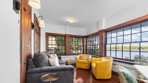 Una habitación con sofá gris, sillones amarillos y vista a un lago a través de amplias ventanas.