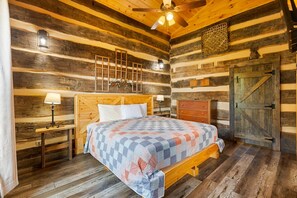 Une chambre à coucher dans un chalet en rondins, avec un lit en bois, une table de chevet, une commode et une porte.