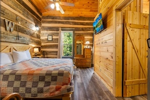 A log cabin bedroom with a bed, a dresser, a ceiling fan, and a window.