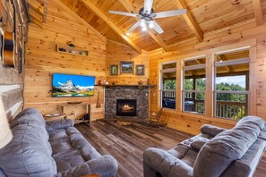 Interior de una cabaña de troncos con chimenea, televisor y sofá.