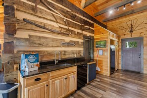 A rustic kitchen with wooden walls, a sink, cabinets, and a refrigerator.