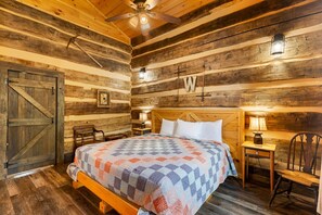 Ein schlicht eingerichtetes Schlafzimmer im Chalet-Stil mit einem Holzbett, einem Nachttisch, einem Sessel und einem Deckenventilator.