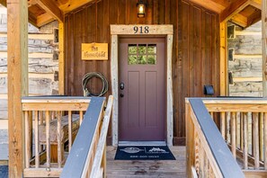 Una cabaña de madera con puerta marrón, un letrero que dice 'The Homestead' y el número '918' sobre la puerta.