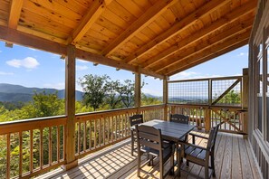 Terraza de madera con mesa y sillas, con vista a un paisaje montañoso.