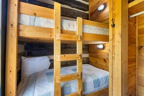 Una cama litera de madera con escalera, un almohadón blanco y una colcha acolchada.