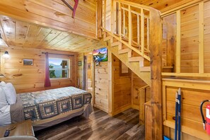 Eine Holzhütte mit einem Bett, einer Treppe und einem Fenster mit Blick auf eine Landschaft.