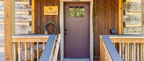 Una cabaña de madera con puerta marrón, un letrero que dice 'The Homestead' y el número '918' sobre la puerta.
