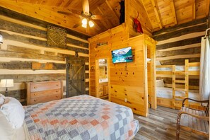 A log cabin interior with a bed, dresser, television, and a wooden ceiling.