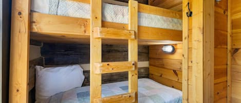 Un lit superposé en bois avec une échelle, un oreiller blanc et une couverture matelassée.