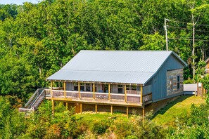 A cabin with a covered porch and a staircase leading up to it, surrounded by dense forest. - The Homestead & The Shed - 2 side-by-side cabins! (Gatlinburg)