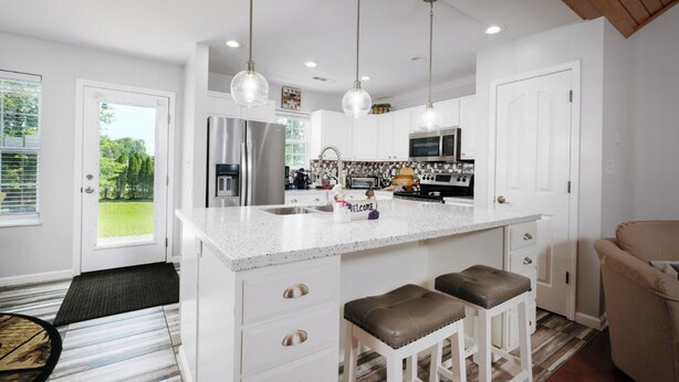 Una cocina moderna con armarios blancos, electrodomésticos de acero inoxidable y una isla grande con taburetes.