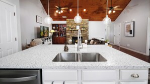 Cocina con una isla grande de granito, pileta de acero inoxidable y lámparas colgantes.