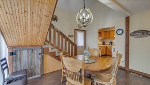 A rustic dining area with a wooden table and chairs, a chandelier, and a staircase leading to a loft. - Grin 'N Bear It - Hot tub, games, and a fireplace! (Sevierville)