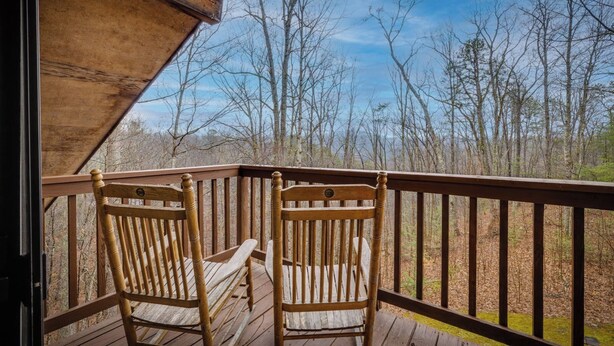 A wooden deck with two wooden chairs, a railing, and a view of leafless trees in the background. - Grin 'N Bear It - Hot tub, games, and a fireplace! (Sevierville)
