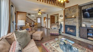 A spacious living room with a fireplace, a dining area, and a staircase. - Grin 'N Bear It - Hot tub, games, and a fireplace! (Sevierville)