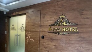 Una entrada de hotel con un muro de madera, una puerta de cristal con un picaporte metálico y un letrero que dice "4 EVER HOTEL" con un símbolo de corona.