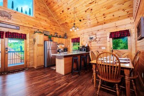 L’intérieur d’un chalet en bois comprend une cuisine, un coin repas et offre une vue sur les montagnes.