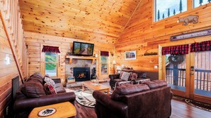 A log cabin interior with a fireplace, leather couches, a television, and a sign reading 'Great Smoky Mountains.'