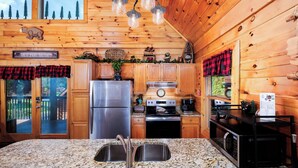 A kitchen with wooden walls, a stainless steel refrigerator, a stove, and a microwave.