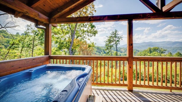 A hot tub on a wooden deck with a view of a forest and mountains.