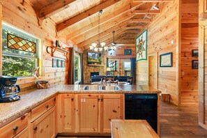 Ein Holzblockhaus-Interieur mit Küchenbereich, der sich durch Granit-Arbeitsplatten, Holzschränke, einen Geschirrspüler und einen Essbereich mit Tisch und Stühlen auszeichnet.