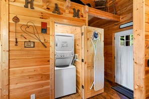 A wooden cabin interior with a built-in washer and dryer, a door with a towel hanging, and a wooden wall with a nameplate.
