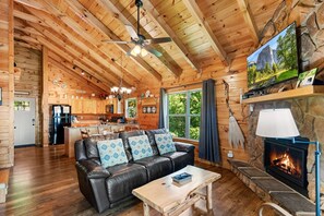 L’intérieur d’une cabane en rondins comprend un salon, une cuisine, une cheminée et une grande fenêtre.
