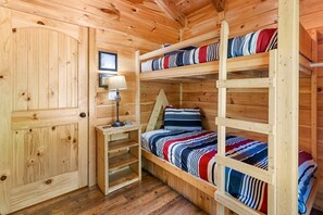 A wooden cabin room with bunk beds, a bedside table with a lamp, and a framed picture on the wall.