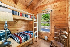 Ein Zimmer in einer Holzhütte mit Etagenbetten, einem Fenster, einem Sessel und einer Lampe.