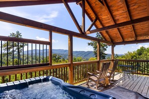 Une terrasse en bois avec un jacuzzi, des sièges d’extérieur et une vue sur les montagnes.