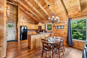 A wooden cabin interior with a kitchen, dining area, and a large window.