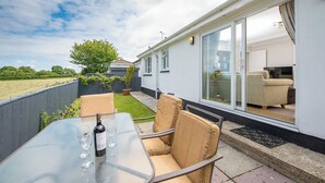 A patio area with a glass table, two chairs, and a bottle of wine. - The Willows Dinas Cross, Holiday Home Dinas, Sleeps 5, 3 bedrooms,  bathrooms (Newport)