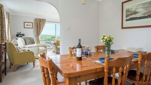 A dining area with a wooden table set for four, a bottle of wine, and a vase of flowers. There is a view of the sea through an archway. - The Willows Dinas Cross, Holiday Home Dinas, Sleeps 5, 3 bedrooms,  bathrooms (Newport)