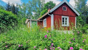 Una casa de madera roja con detalles blancos, rodeada de exuberante follaje y flores silvestres.