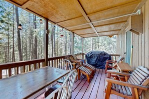 Una terrassa de fusta amb taula i cadires, una barbacoa i vista al bosc.