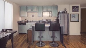 Cozinha moderna com armários azul claro, ilha central com banquetas, eletrodomésticos de aço inoxidável e piso de madeira.