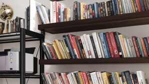 Um espaço de trabalho moderno com uma cadeira preta e uma escrivaninha, rodeado por estantes cheias de livros e um globo.