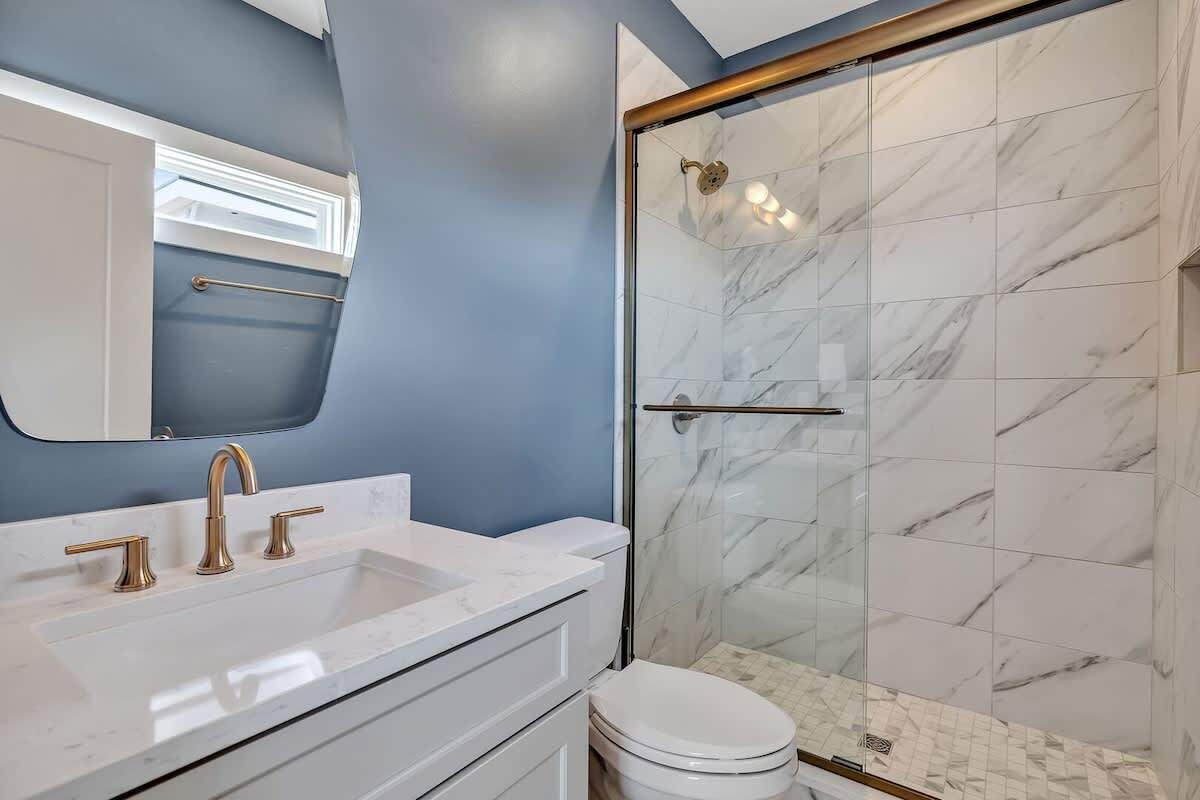 A bathroom with a white sink, a toilet, and a glass-enclosed shower with marble tiles.