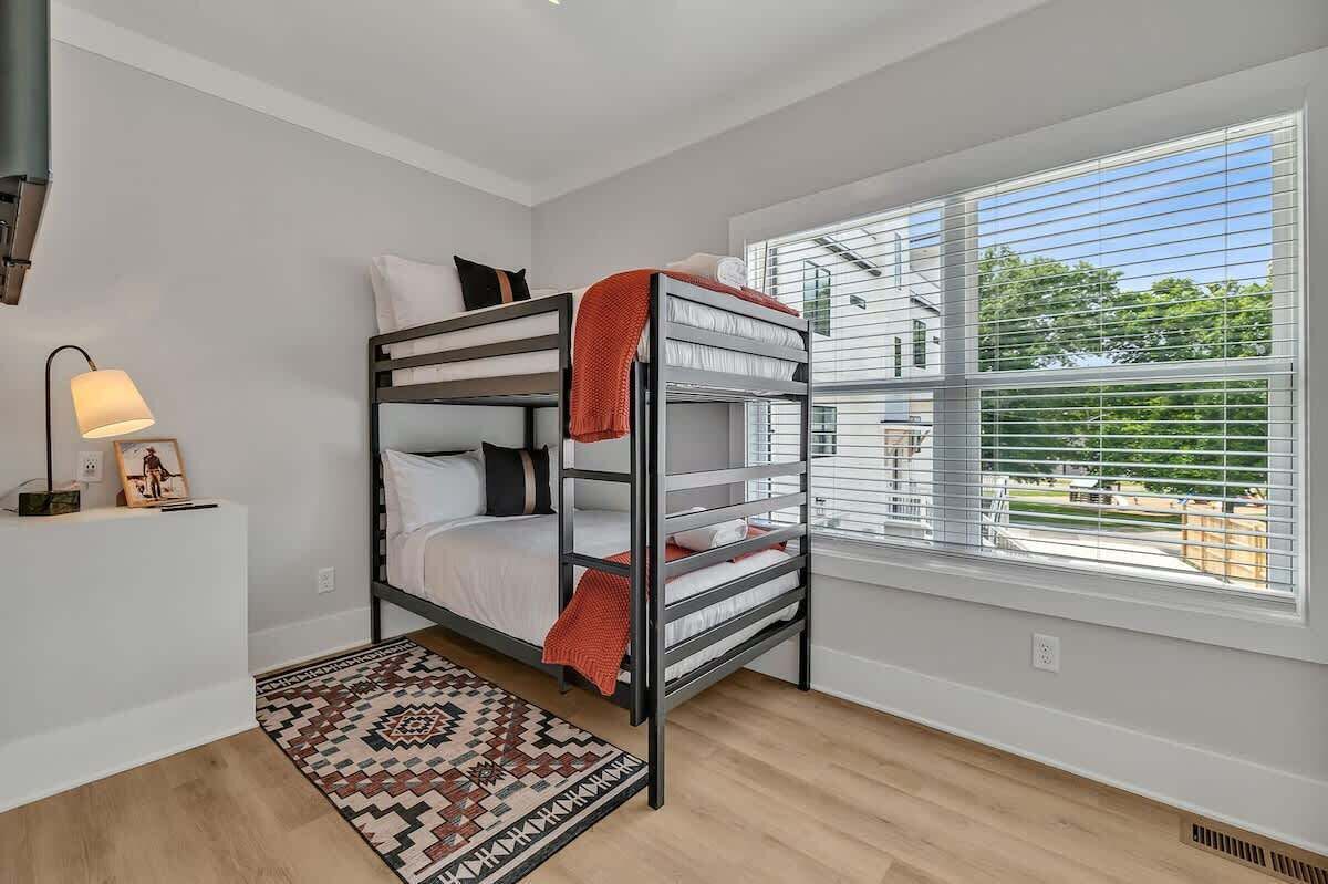 A bunk bed room with a window, a lamp, and a patterned rug.