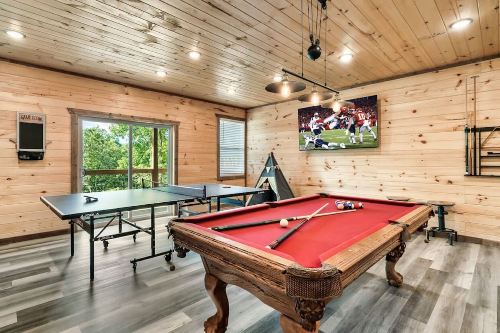 A wooden room with a pool table, a ping pong table, and a billiards table.