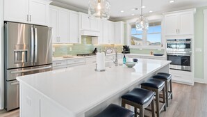 A modern kitchen with white cabinets, stainless steel appliances, and a large island with bar stools. - NOW AVAILABLE BRAND-NEW! Private beach home with incredible views! (Ocean Isle Beach)