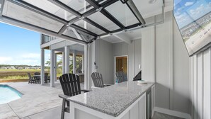 A modern kitchen with a large island, a glass enclosure, and a view of the outdoors. - NOW AVAILABLE BRAND-NEW! Private beach home with incredible views! (Ocean Isle Beach)