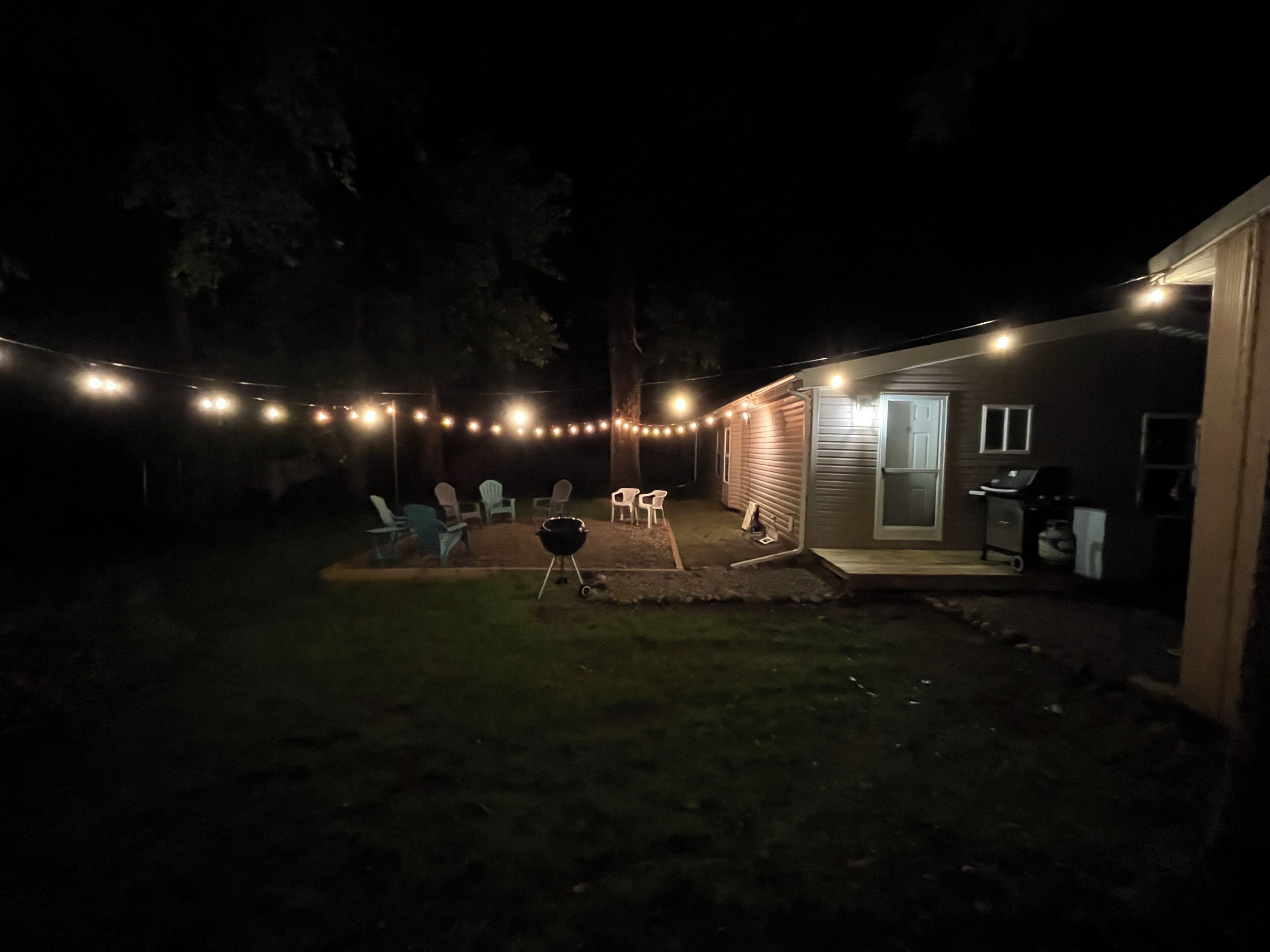 A backyard with string lights, a grill, and outdoor seating.