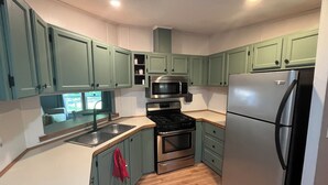 Cocina compacta con armarios verde azulado, un refrigerador de acero inoxidable, un microondas y una estufa.