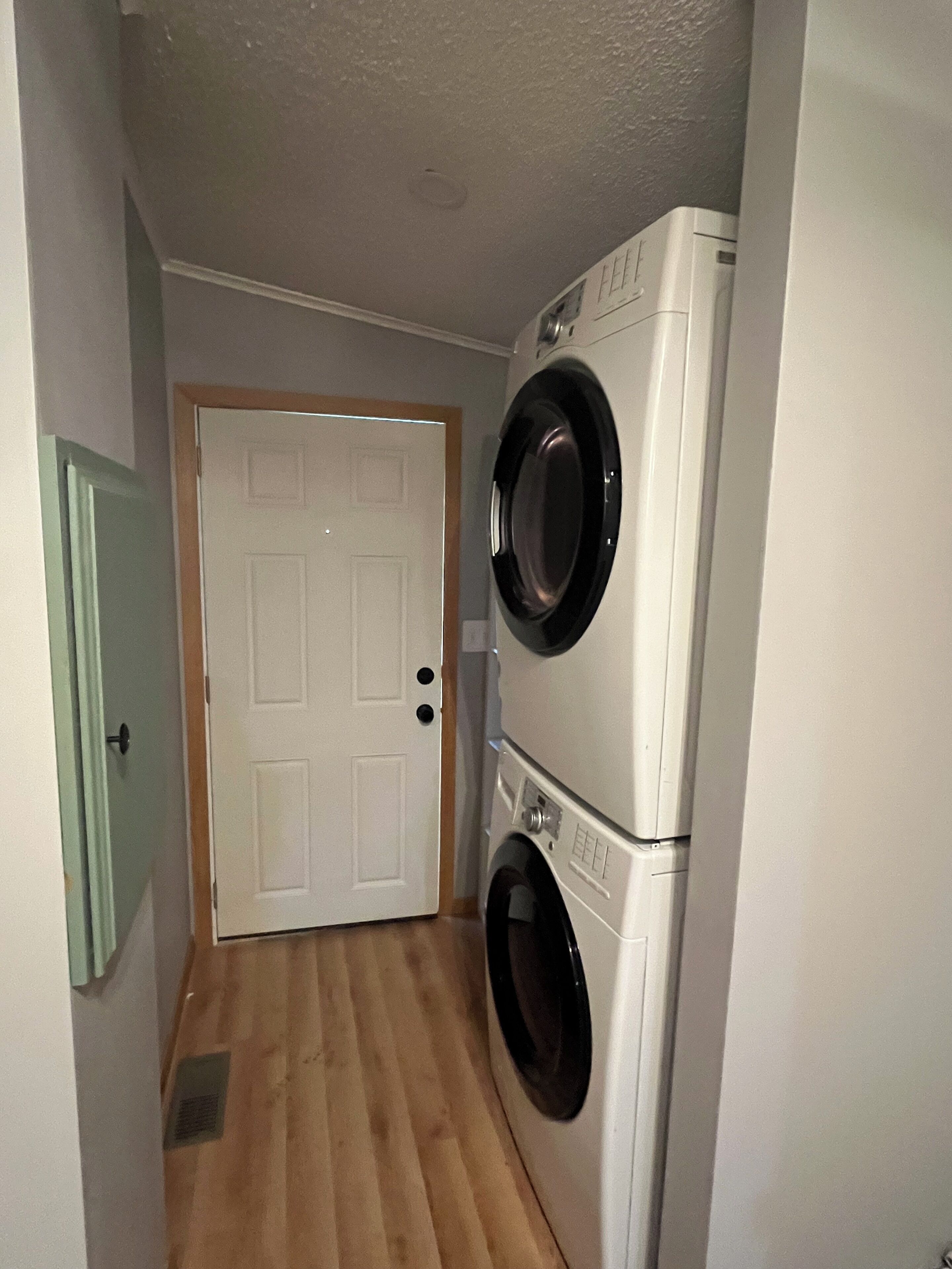 Una sala de bugaderia amb dues piles de rentadores i assecadores, un terra de fusta i una porta blanca.