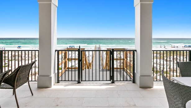 A beach view from a covered patio with a railing, chairs, and a table. - Luxurious Beachfront Retreat: Pool, Spa, Chefs Kitchen (Destin)