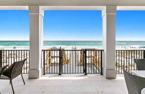 A beach view from a covered patio with a railing, chairs, and a table. - Luxurious Beachfront Retreat: Pool, Spa, Chefs Kitchen (Destin)