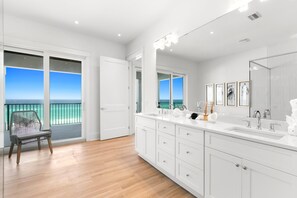 A modern bathroom with a large mirror, white cabinetry, and a view of the ocean through large windows.