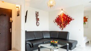 Ein modernes Wohnzimmer mit einem schwarzen Ledersofa, einem Glastisch mit Obstschale, einer Kronleuchter und einem leuchtend roten Kunstwerk an der Wand.